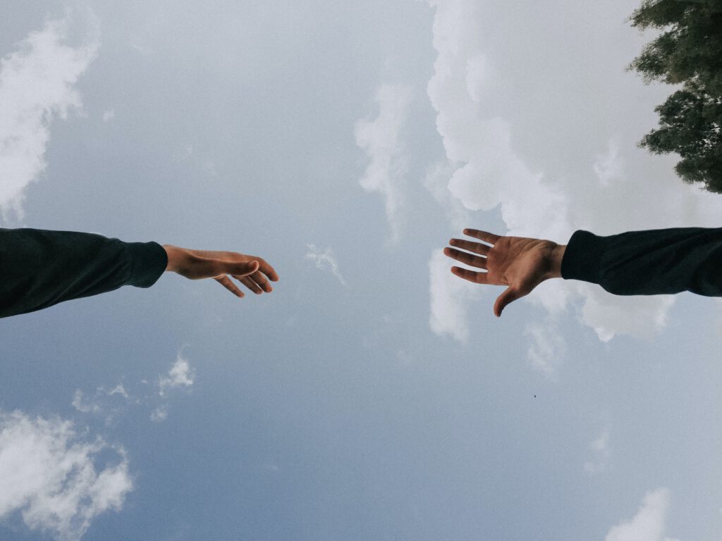 Zwei Hände sind zueinander ausgestreckt vor blauem Himmel mit Wolken
